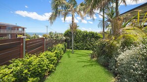 A well-maintained garden with a clear pathway, palm trees, and a view of the ocean. - Paradise on Partridge (Port Macquarie)