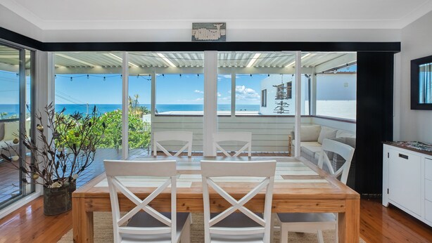 A dining area with a wooden table and white chairs, overlooking a pool and ocean view. - Paradise on Partridge (Port Macquarie)