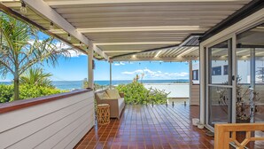 A covered patio with a tiled floor, a wicker sofa, and a view of the ocean. - Paradise on Partridge (Port Macquarie)