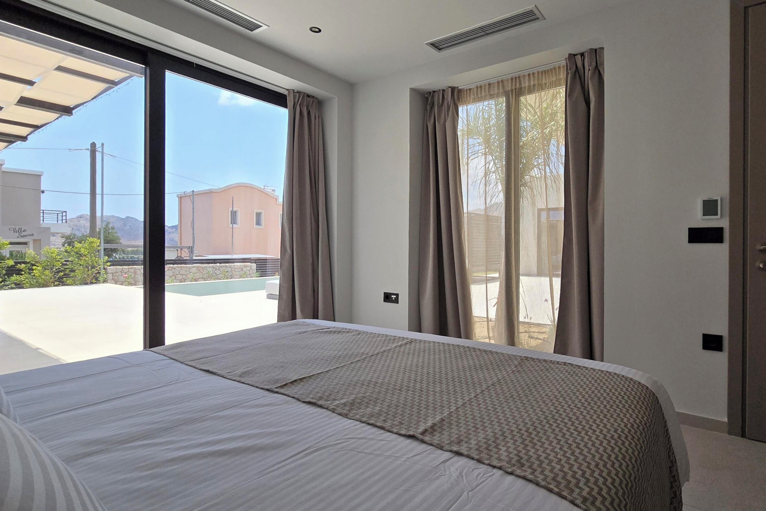 Ein Hotelzimmer mit einem großen Bett, einer Schiebetür zum Außenbereich und Blick auf Gebäude und einen Pool.