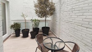 A small outdoor seating area with a glass table and wicker chairs, surrounded by potted plants and a white brick wall. - GLOBAL Apartments & Rooms (L'Hospitalet de Llobregat)