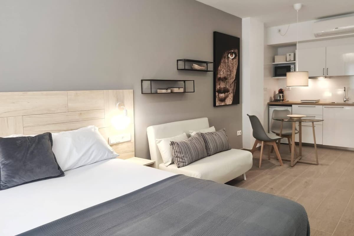 Una habitación de hotel moderna con cama, mesita de noche y una pequeña cocina.