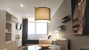 A modern hotel room with a bed, a glass dining table, a chair, a wardrobe, a TV, a large window, and a painting on the wall. - GLOBAL Apartments & Rooms (L'Hospitalet de Llobregat)
