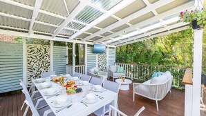 An outdoor patio with a table set for a meal, surrounded by white chairs and a white sofa.