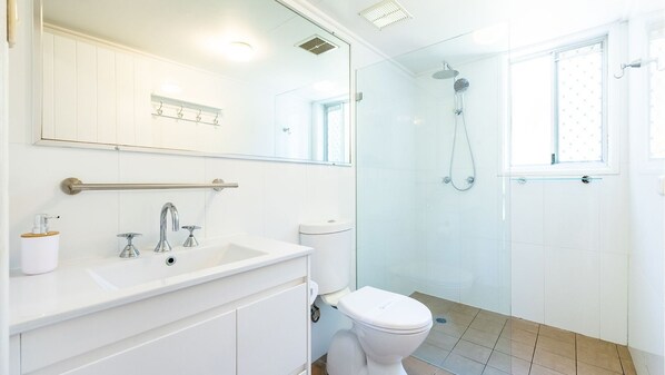 A modern bathroom with a glass-enclosed shower, a white sink with a soap dispenser, and a toilet.