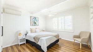 Une chambre à coucher comprenant un lit, un ventilateur de plafond, une fenêtre avec des stores, une chaise et un climatiseur fixé au mur.