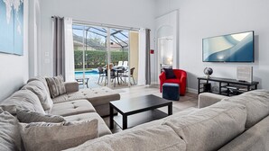A modern living room with a sofa, a coffee table, and a TV. There is a pool visible through the glass doors. - The Hideaway@Tuscan Hills, a modern 4 bedroom, 3 bath luxury home (Davenport)