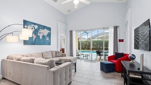 A spacious living area with a large sofa, a red armchair, and a coffee table. There is a world map on the wall, a globe on a side table, and a ceiling fan. - The Hideaway@Tuscan Hills, a modern 4 bedroom, 3 bath luxury home (Davenport)