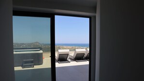 Ein Zimmer mit einer Schiebeglastür, die auf eine Terrasse mit Sitzgelegenheit und Meerblick führt.
