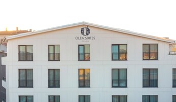 Un edificio con un letrero que dice "Olea Suites Gemlik". Tiene varias ventanas con balcones y un techo plano.