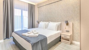 Habitación de hotel moderna con una cama grande, una mesita de noche con lámpara y vistas al exterior a través de la ventana.