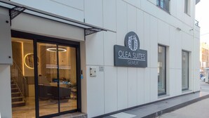 Entrada de un hotel con un cartel que dice "Olea Suites Gemlik" y un interior moderno visible a través de puertas de vidrio.