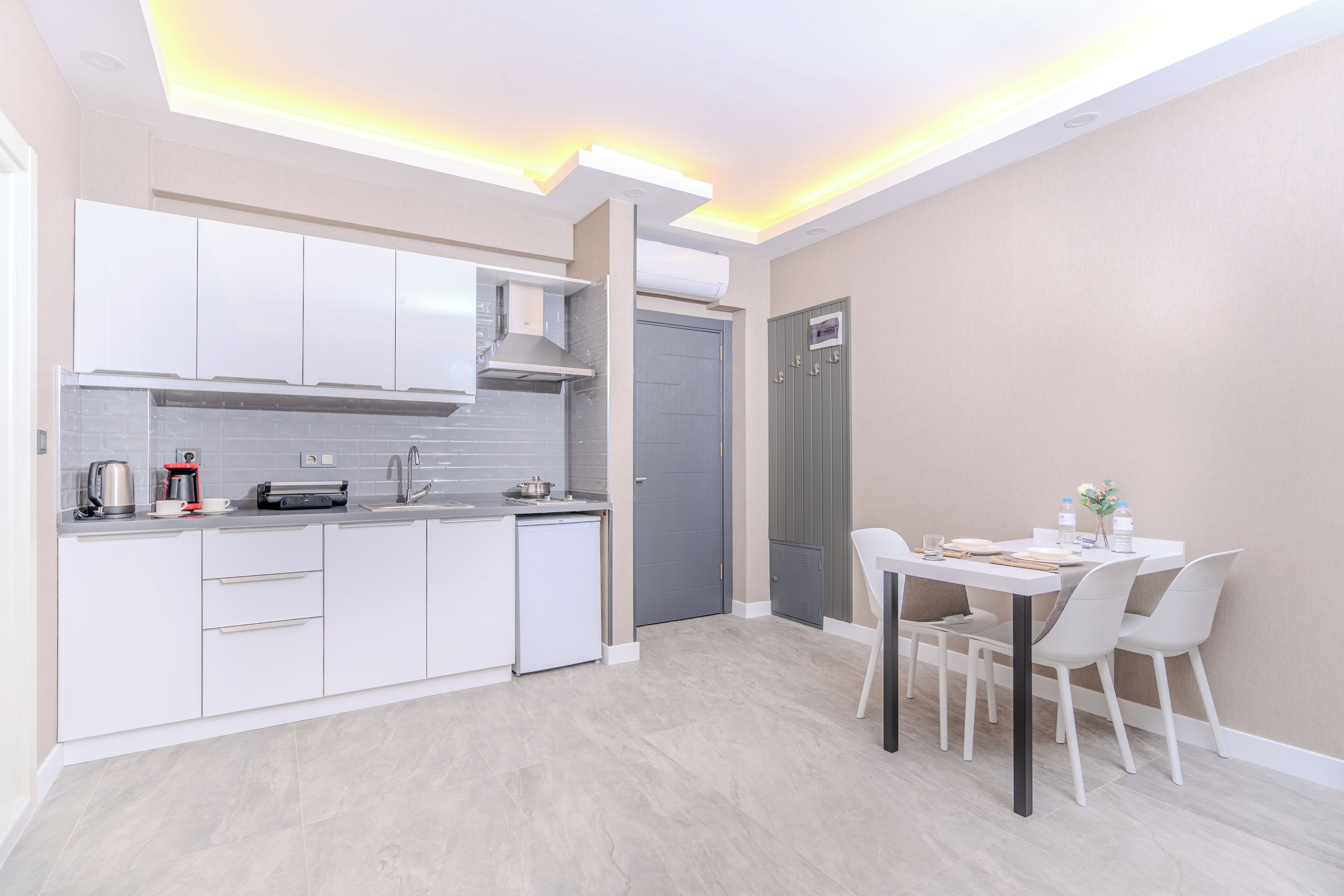 Una cocina moderna con armarios blancos, horno empotrado y comedor con mesa y sillas.