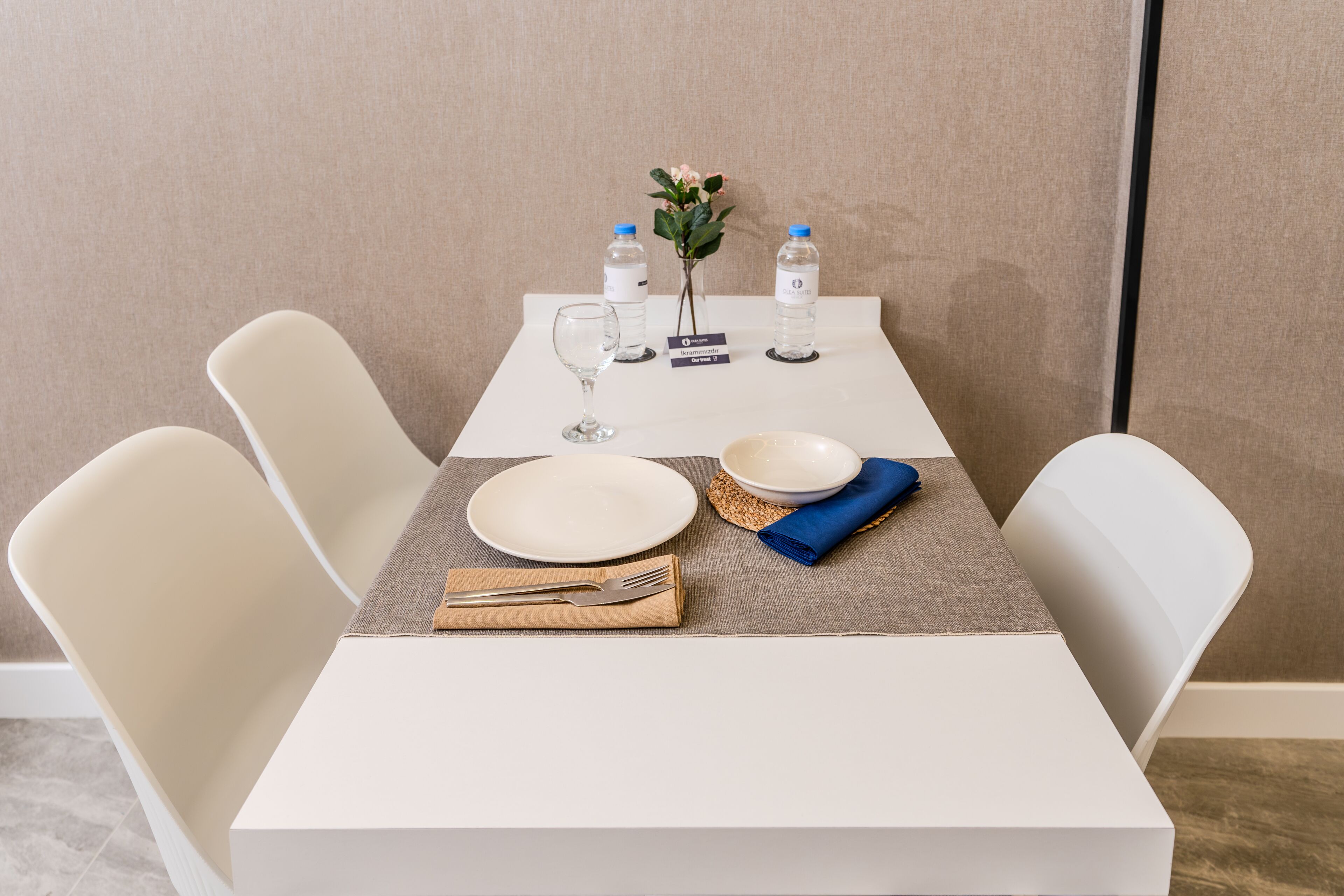A neatly set dining table with white chairs, a vase with flowers, water bottles, and a name card.