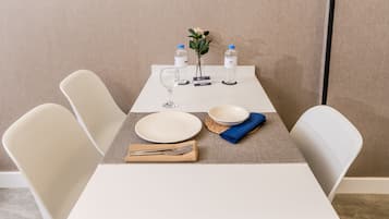 Una mesa de comedor bien dispuesta, con sillas blancas, un florero con flores, botellas de agua y una tarjeta con nombre.