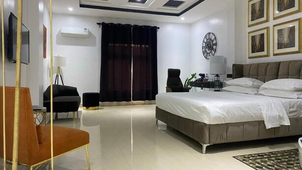 A modern bedroom with a large bed, a desk, a chair, and a TV. - Nevada Hotels and Suites Lekki (Lekki)