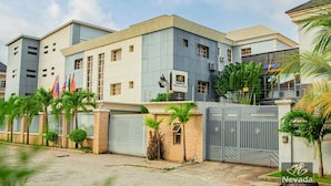 A modern hotel with a two-story structure, multiple flags, and a lounge area. - Nevada Hotels and Suites Lekki (Lekki)