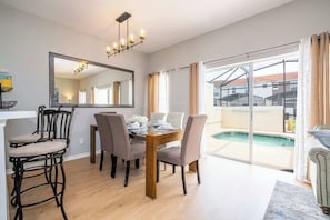 A dining area with a table, chairs, a chandelier, and a view of a swimming pool.