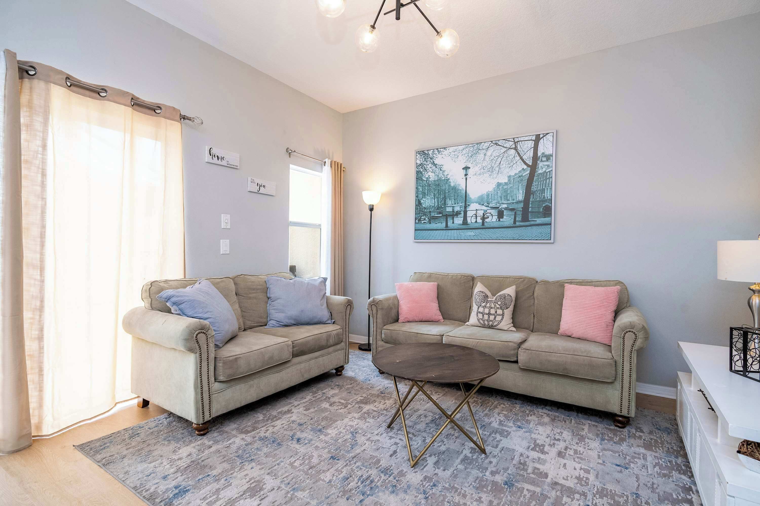 A living room with two beige sofas, a coffee table, a painting on the wall, and a floor lamp.