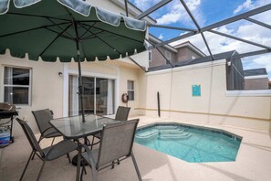 A glass-enclosed patio with a pool, outdoor furniture, and a green umbrella. - Stylish 4BR Townhome - Private Pool, BBQ & Near Disney (Kissimmee)