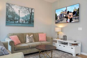 A living room with a sofa, a coffee table, a TV, and a lamp. - Stylish 4BR Townhome - Private Pool, BBQ & Near Disney (Kissimmee)