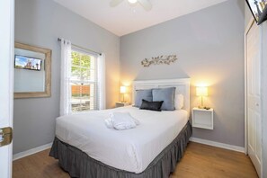 A neatly made bed with a white comforter and a skirted bed skirt, two bedside lamps, a framed picture on the wall, and a window with blinds. - Stylish 4BR Townhome - Private Pool, BBQ & Near Disney (Kissimmee)