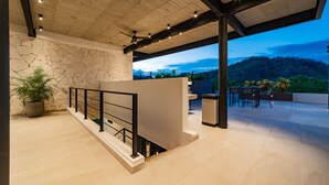 Un espacio exterior moderno con un muro de piedra, techo de madera y vista a una montaña.