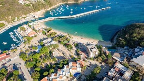 Vista aérea de un pueblo costero con puerto deportivo, playa y edificios.
