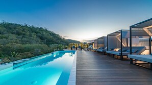 Zona de piscina con terraza de madera, sillas de descanso y vista a un paisaje boscoso.