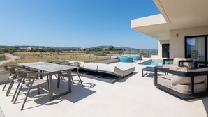 A modern outdoor patio with a pool, seating, and a view of the countryside. - Trapezia Luxury Living - Turquoise (Afantou)