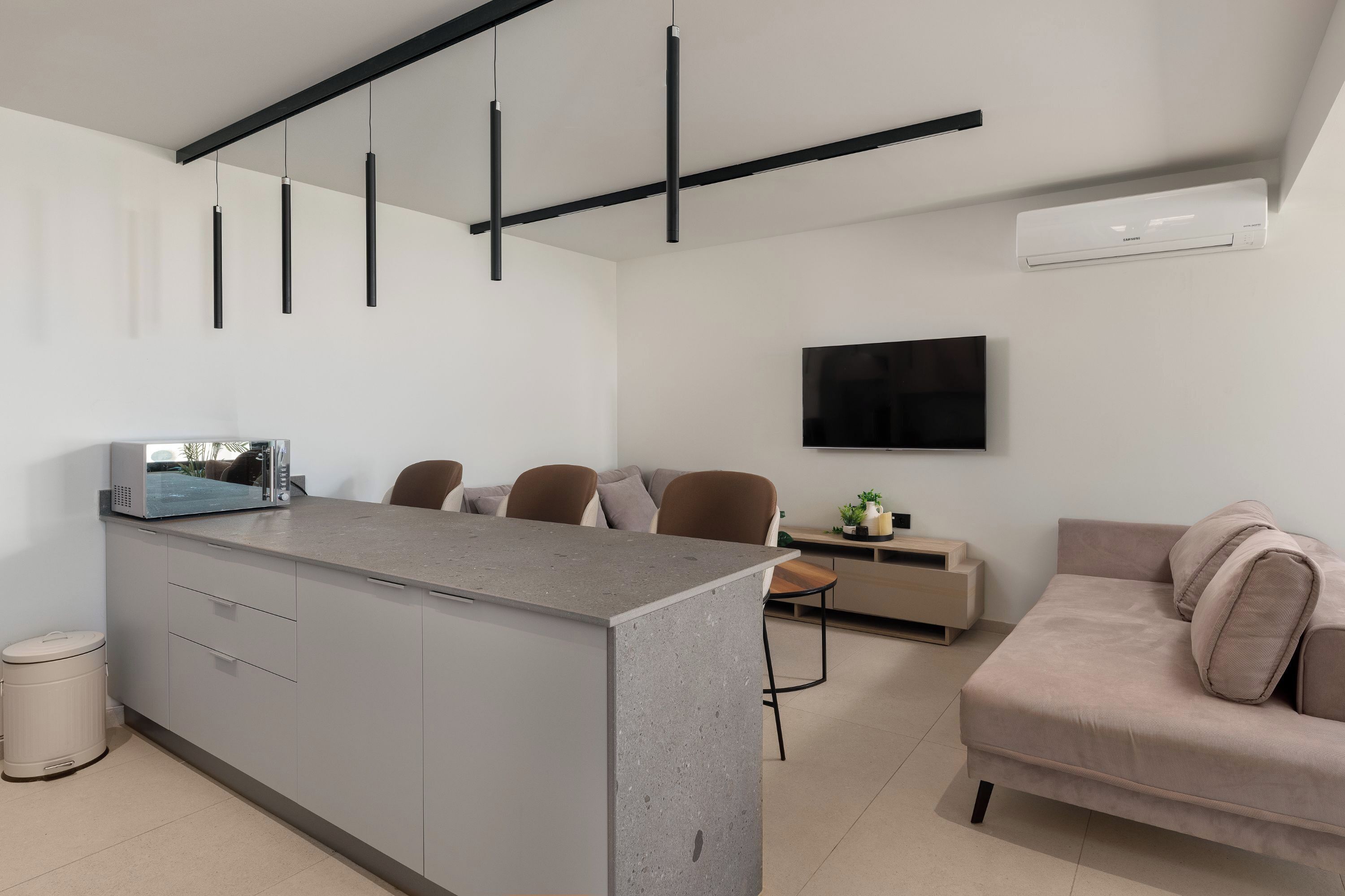 Une cuisine moderne avec un îlot central, un coin repas avec des chaises, un canapé, un téléviseur fixé au mur et une poubelle.