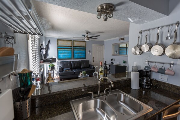A modern kitchen with a double sink, a ceiling fan, and a dining area with a black leather couch.