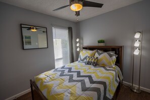 A bedroom with a bed, a ceiling fan, a mirror, a window with blinds, and a bedside lamp. - I14 - Apt|Patio|11mi to Convention Ctr|Sleeps 4 (Irving)