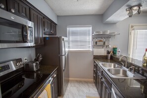 A modern kitchen with stainless steel appliances, a granite countertop, and a window with blinds.