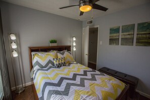 A bedroom with a bed, bedside lamps, a ceiling fan, a door, and wall art.