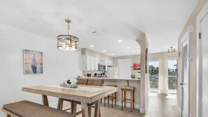 Une cuisine moderne avec des meubles blancs, une table à manger en bois avec des bancs et un luminaire suspendu.