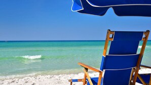 Uma cadeira de praia e um guarda-sol numa praia arenosa com águas turquesa cristalinas e céu claro.