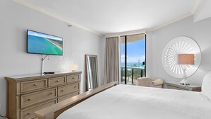 Quarto de hotel com cama, televisão, cômoda, cadeira, abajur e vista para o exterior.
