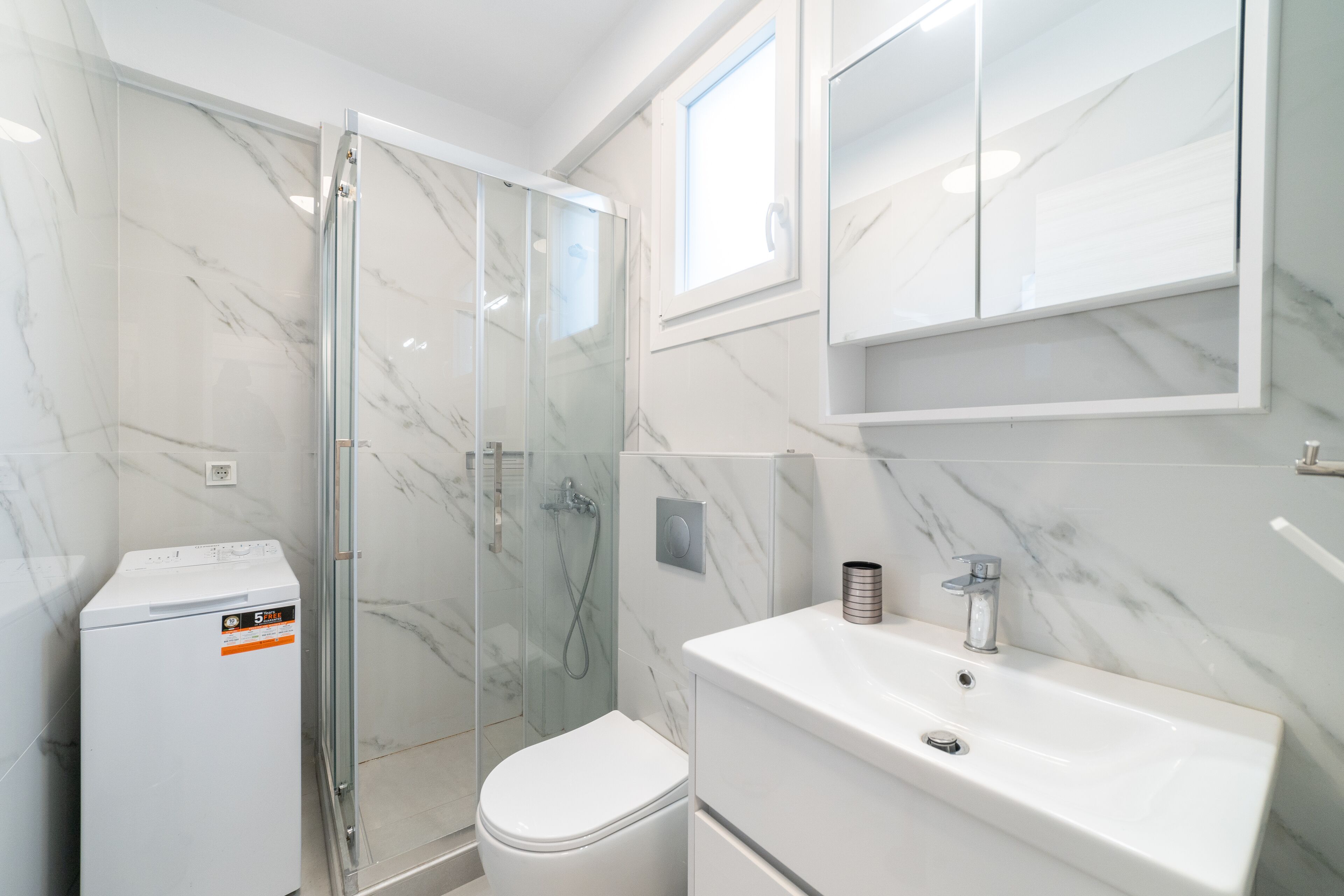 Een moderne badkamer met een glazen douchecabine, een wit toilet en een wastafel met spiegel.