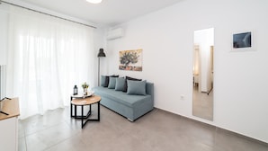 A modern living room with a grey sofa, a small round table, and a floor lamp. - Antigone Residential Complex (Pangaio)