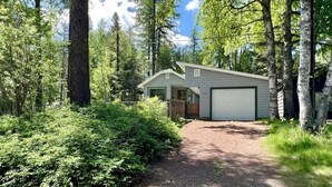 A single-story house with a garage, surrounded by dense forest. - Wonderful West Glacier Basecamp Property (Columbia Falls)