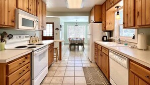 A kitchen with wooden cabinets, a microwave, stove, and dishwasher. There is a dining table with chairs in the background. - Wonderful West Glacier Basecamp Property (Columbia Falls)