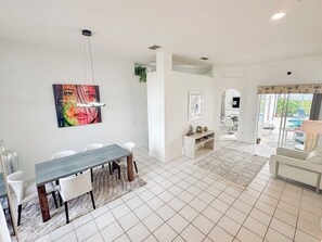A spacious living area with a dining table, white chairs, a TV, and a view of the outdoors. - Grand Exclusive 4BR Grove Home near Disney (Four Corners)