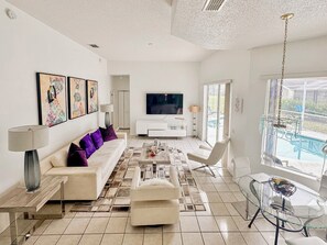 A modern living room with a sofa, coffee table, TV, and a glass table with chairs. - Grand Exclusive 4BR Grove Home near Disney (Four Corners)