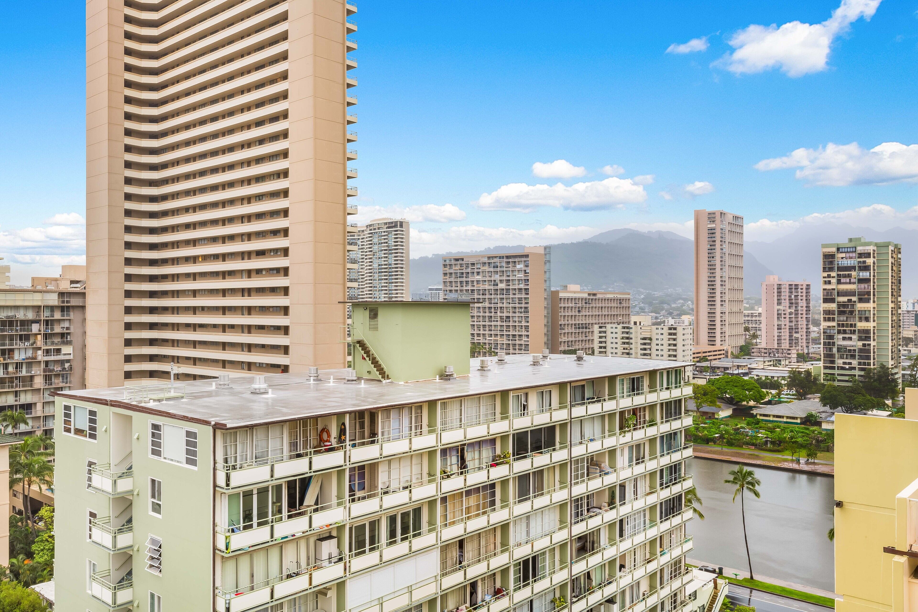 A multi-story building with balconies, a flat roof, and a view of a cityscape with mountains in the background.