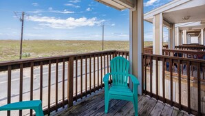 Une terrasse en bois avec un fauteuil Adirondack turquoise et un tabouret assorti, donnant sur une route et un paysage ouvert.
