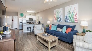 Un salon moderne avec un canapé bleu, une table basse en bois et un coin cuisine à l’arrière-plan.
