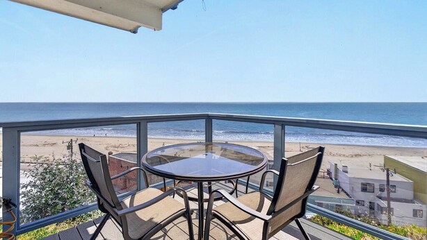 Un balcon avec une table et des chaises en verre donnant sur une plage.