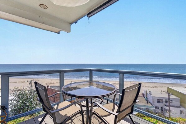 Un balcon avec une table et des chaises en verre donnant sur une plage.