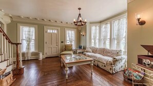 A spacious living room with hardwood floors, a chandelier, a sofa, a chair, and a coffee table. - The 1840's Goat House (Elburn)